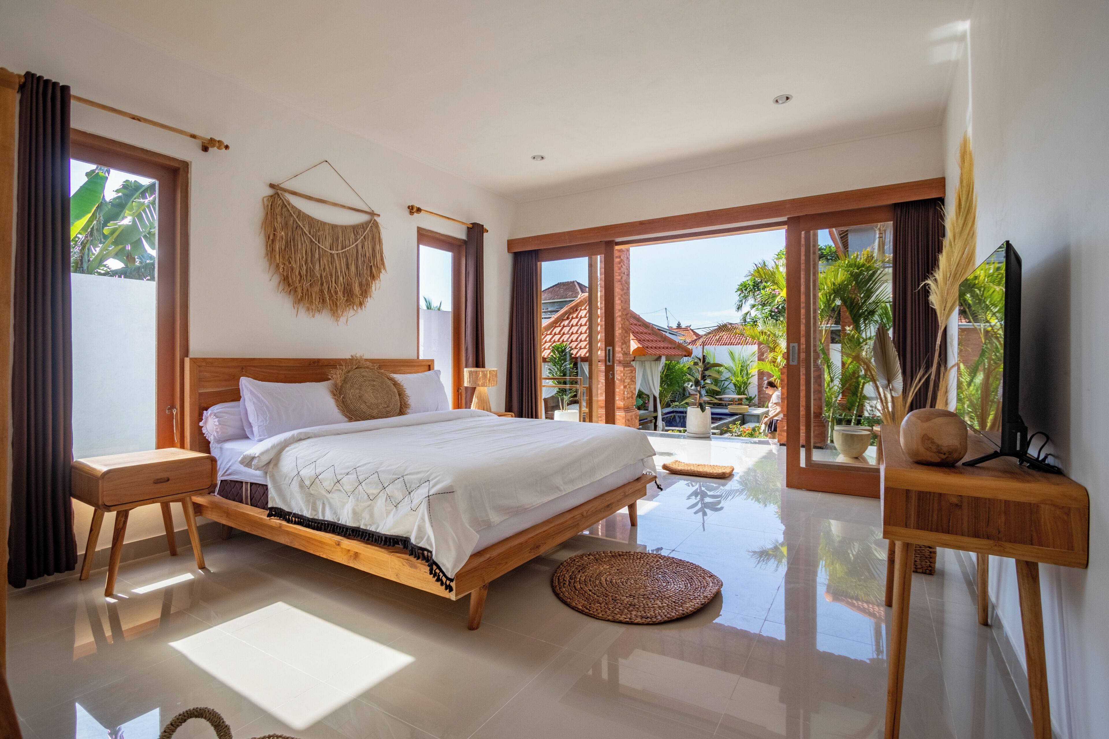 A spacious bedroom with a large bed, wooden nightstands, a TV, and a view of the outdoors.