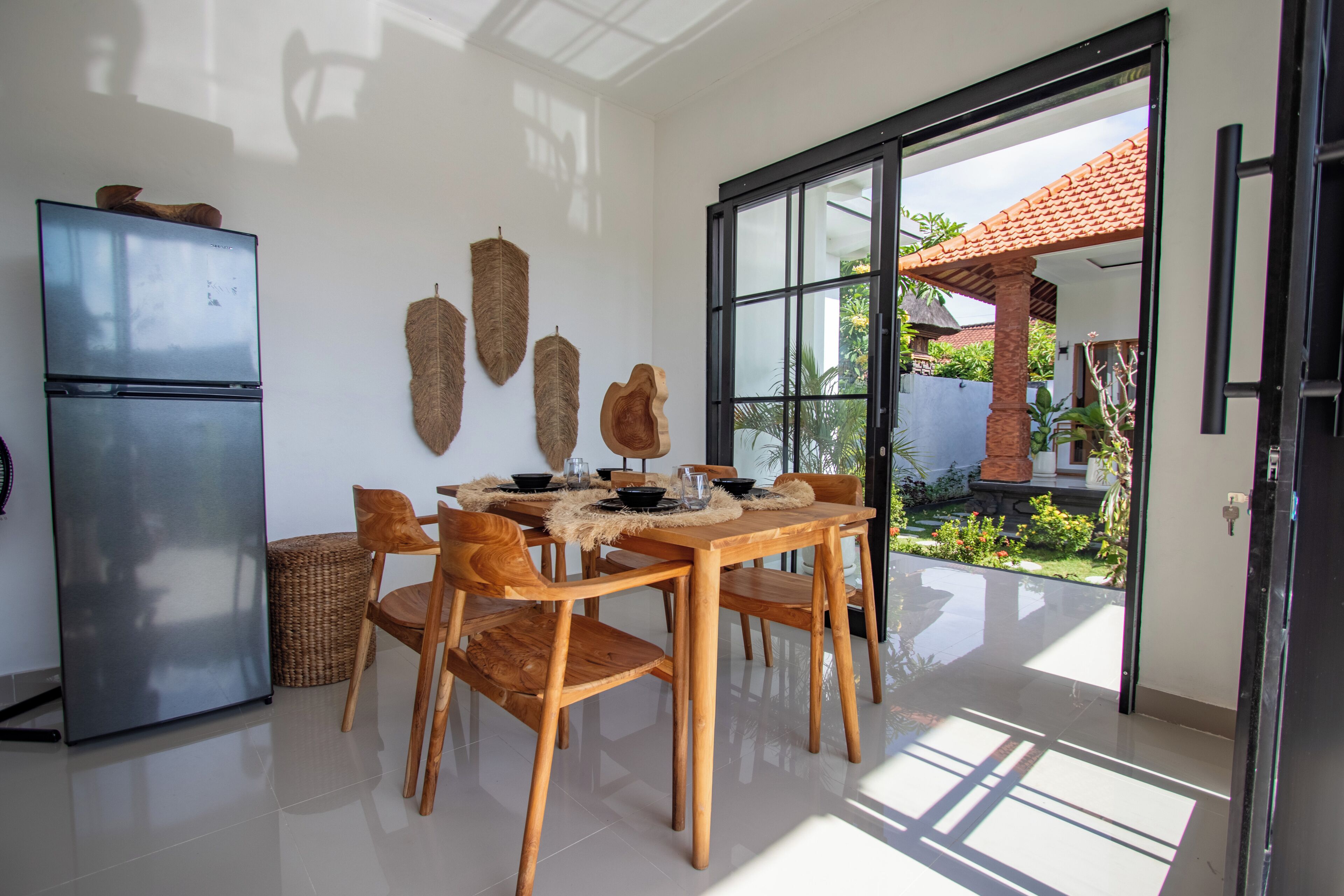 A dining area with a wooden table, chairs, a refrigerator, and woven wall decorations.