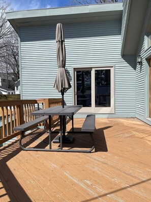 A deck with a picnic table and umbrella, a sliding glass door, and a light blue exterior wall. - 2-Minute Walk to Main Street & Mirror Lake, 2BR Apt overlooking Mirror Lake (Lake Placid)