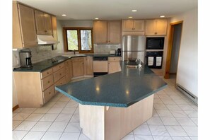 A kitchen with wooden cabinets, a granite countertop, stainless steel appliances, and a tiled floor. - 2-Minute Walk to Main Street & Mirror Lake, 2BR Apt overlooking Mirror Lake (Lake Placid)