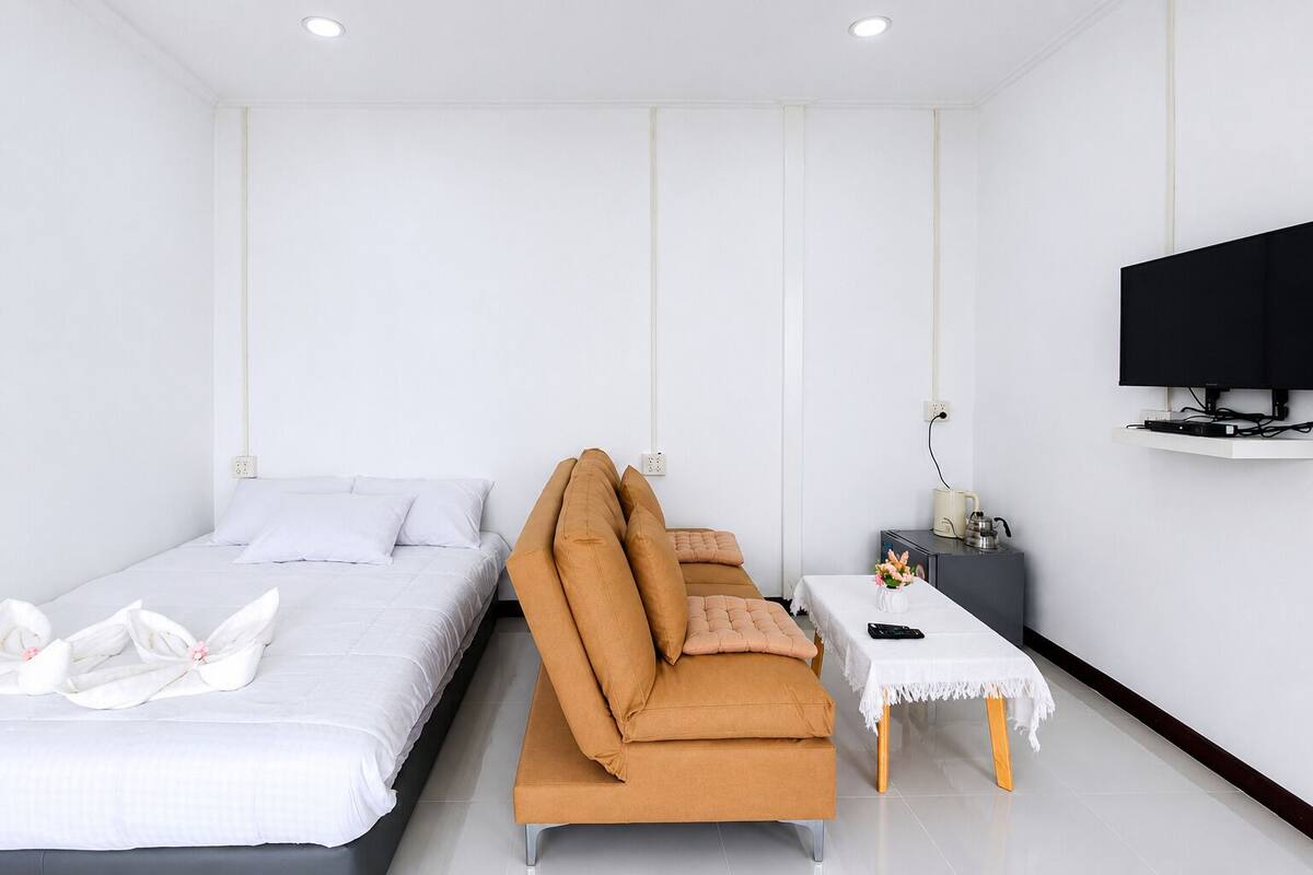 A hotel room with a bed, a sofa, a small table with a lamp, and a TV mounted on the wall.
