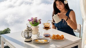 A woman pouring coffee into a cup at a table with a view of clouds, a lantern, and flowers. - A View Khao Soon  (Chawang)