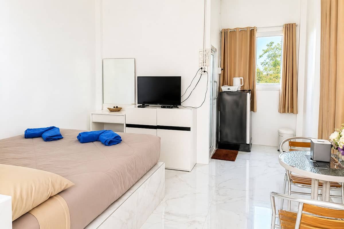 A hotel room with a bed, a TV, a desk, a refrigerator, a coffee maker, and a dining area with a table and chairs.