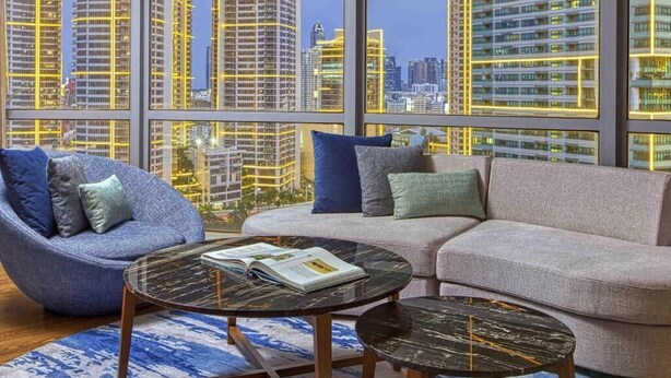 A modern living room with a sofa, armchair, and coffee table, large windows with city views, and a patterned rug. - Novotel Suites at Acqua (Mandaluyong)