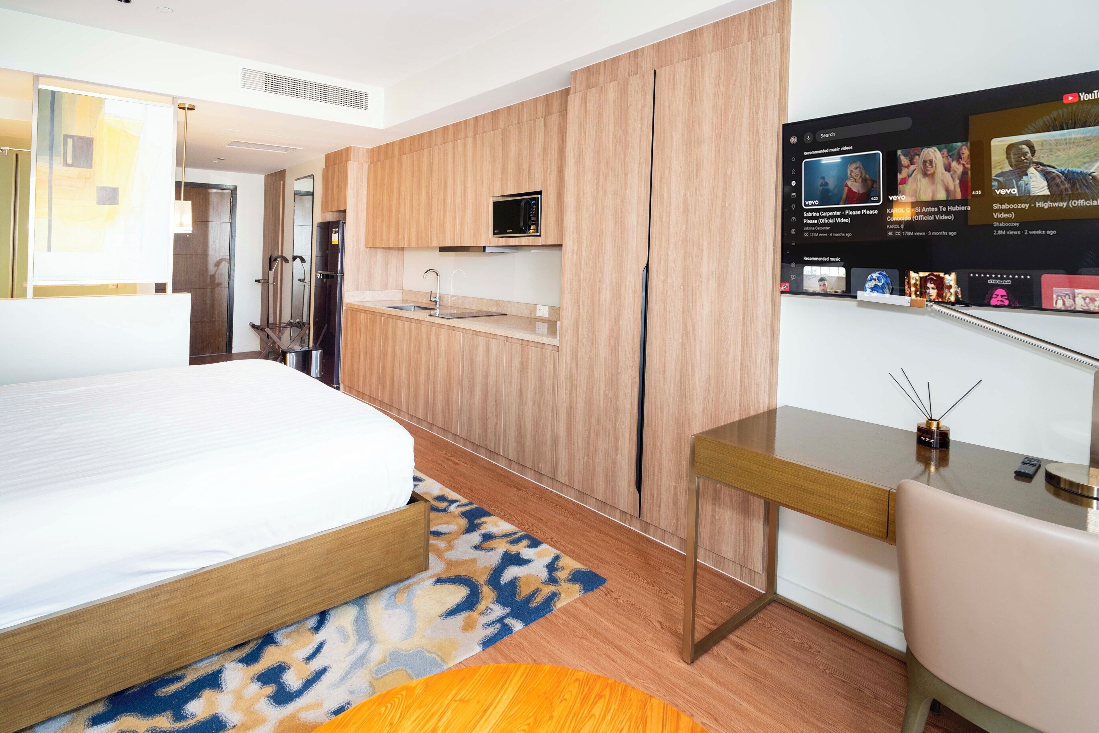 Habitación de hotel moderna con cama, escritorio, televisor montado en la pared y microondas incorporado.