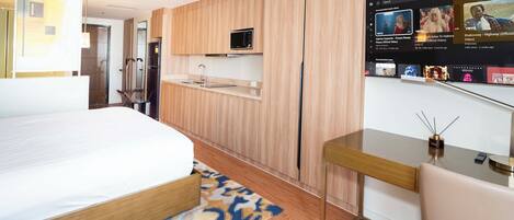 Habitación de hotel moderna con cama, escritorio, televisor montado en la pared y microondas incorporado.