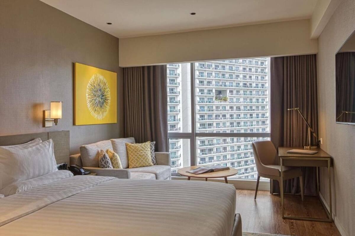 Une chambre d’hôtel avec un grand lit, un canapé, un bureau et une vue sur un immeuble de grande hauteur.