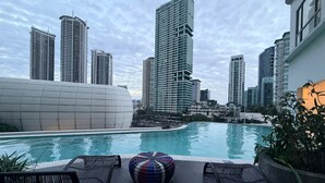A rooftop pool with lounge chairs and a colorful ottoman, surrounded by high-rise buildings. - Novotel Suites at Acqua (Mandaluyong)