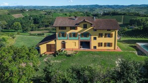 Una casa de dos pisos con techo de tejas, rodeada de campos verdes y colinas.