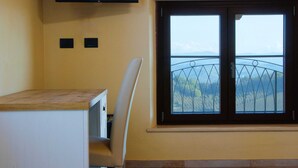 Una habitación con un escritorio de madera, una silla blanca, un televisor montado en la pared y una ventana con vistas a las montañas.
