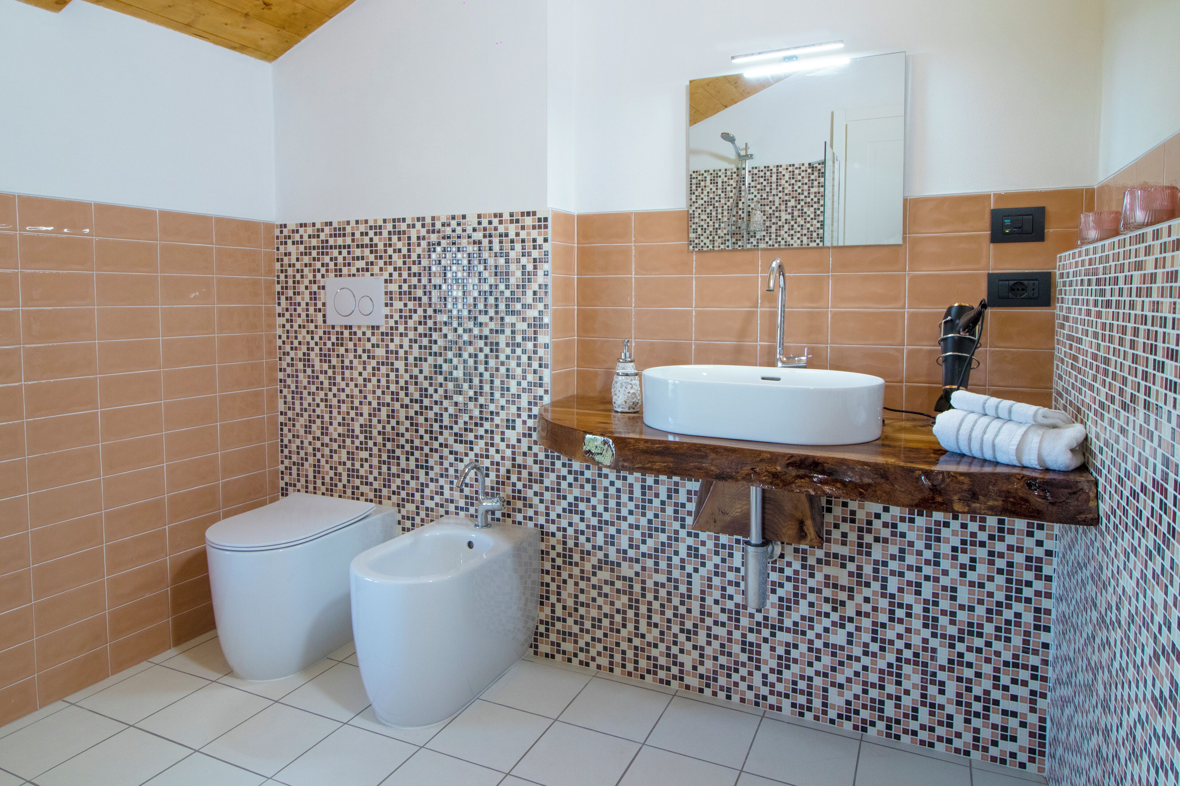 A bathroom with a toilet, bidet, and sink with a wooden countertop.