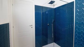 Un bagno con box doccia in vetro, porta bianca e piastrelle a motivi blu.