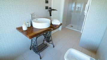 Een badkamer met een houten wastafel, een witte wasbak, een douche en een toilet.
