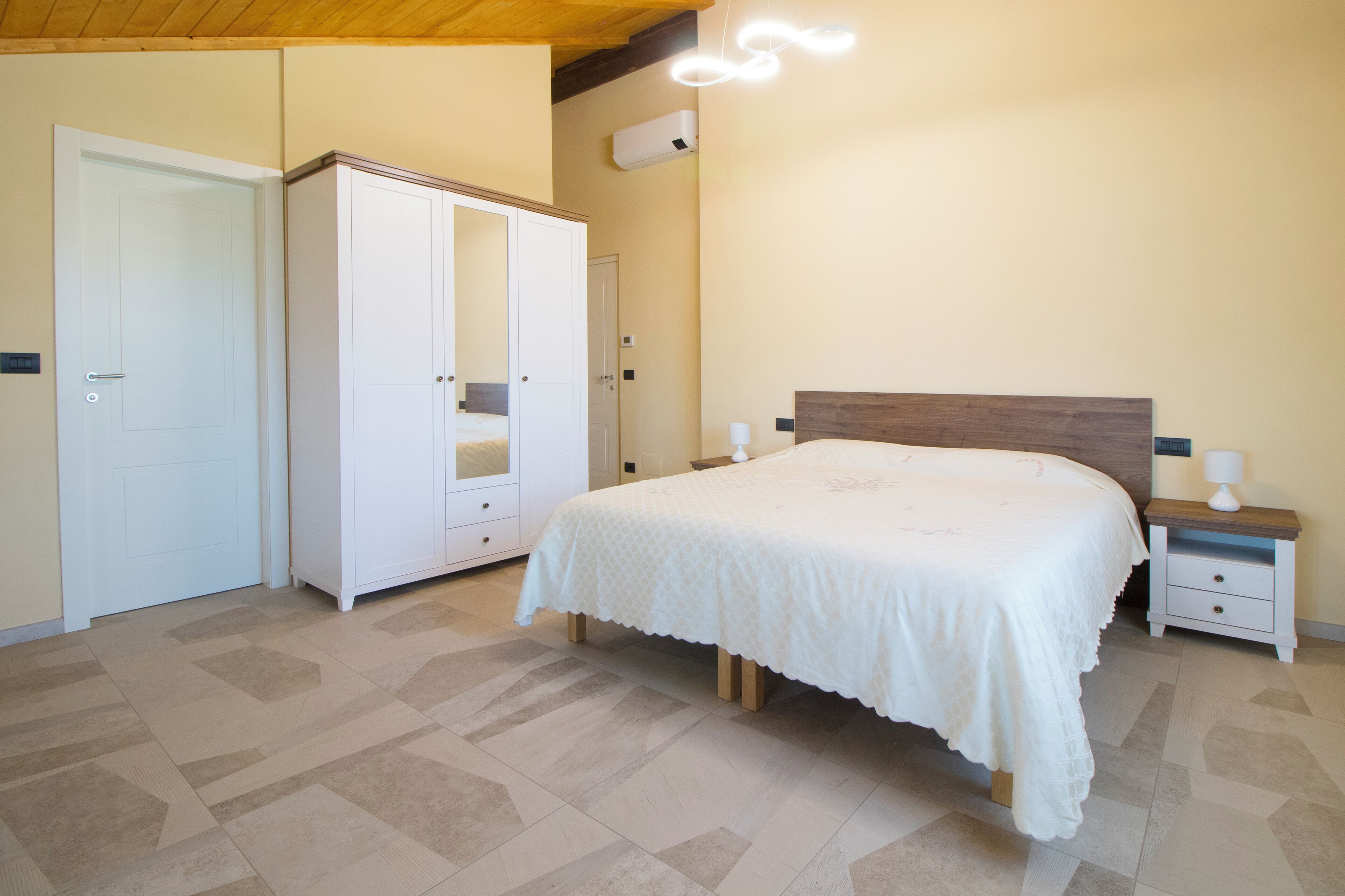 Un dormitorio con cama, armario, mesita de noche y lámpara en el techo.
