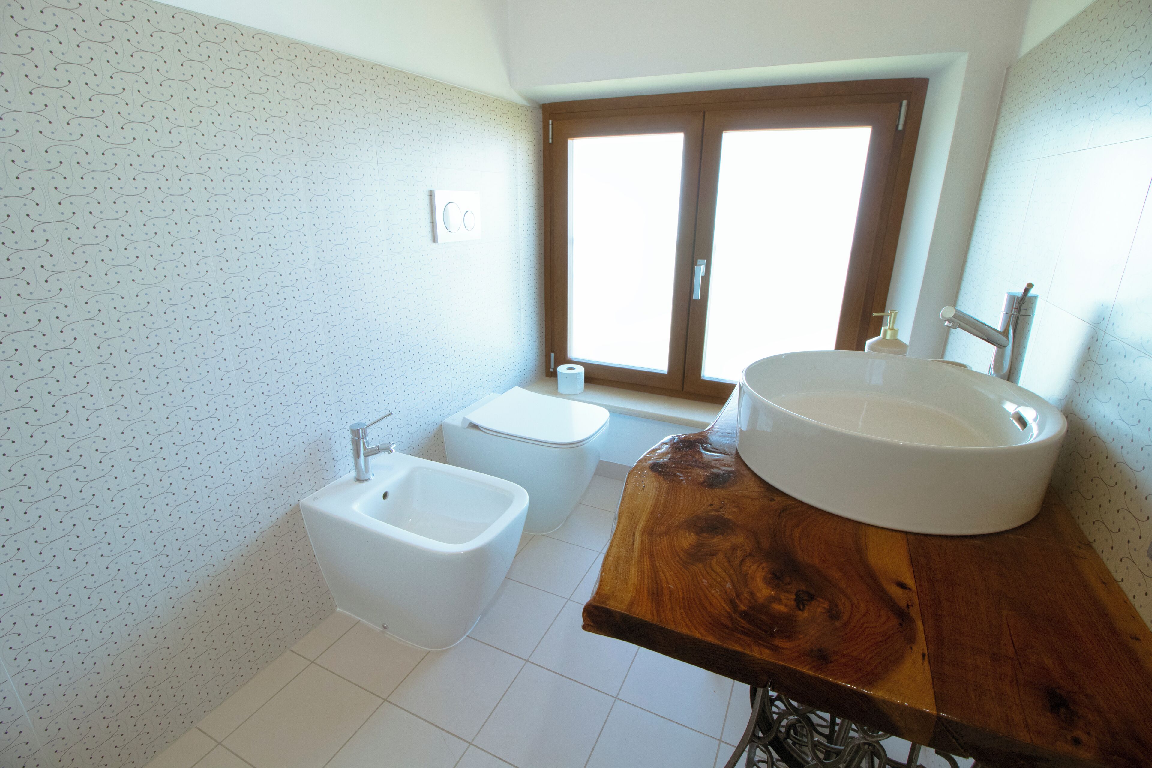 A bathroom with a wooden vanity, a bidet, a toilet, and a window with a view.