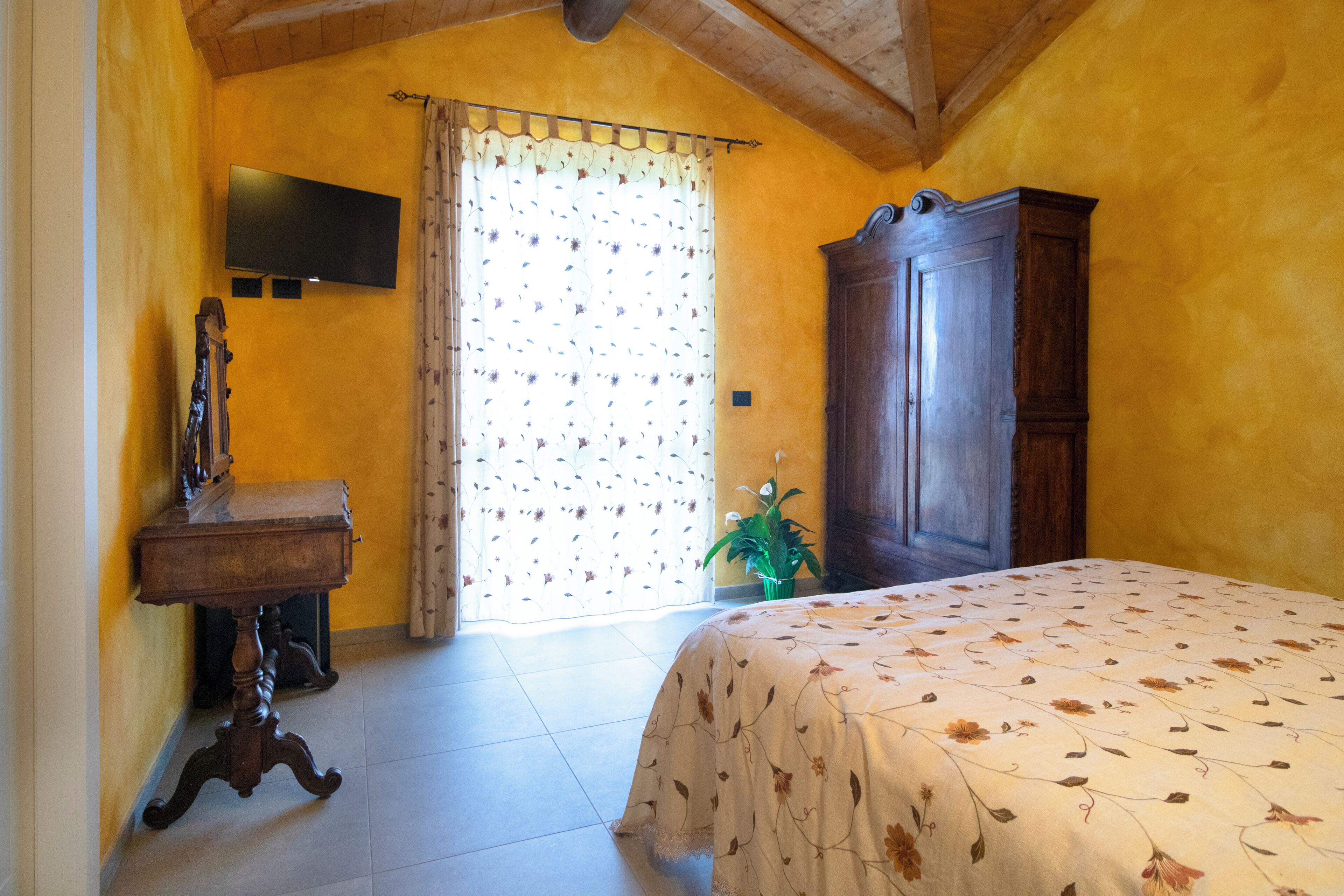 A bedroom with a bed, a wooden cabinet, a television on the wall, and a window with curtains.