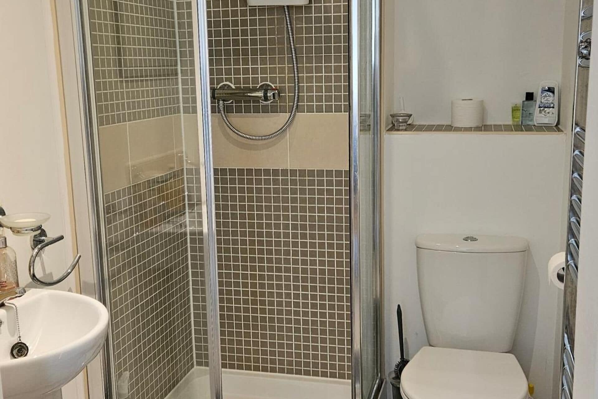 Un bagno con cabina doccia in vetro, un water bianco e un lavabo con rubinetto cromato.