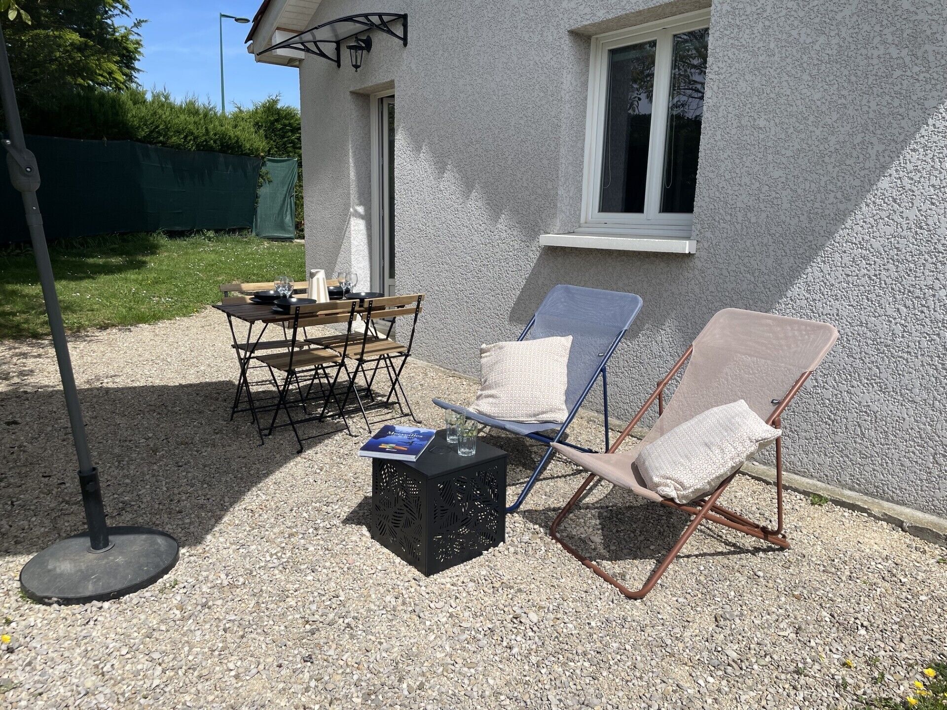 Une terrasse avec une table et des chaises, un petit pot de fleurs noir et deux fauteuils de jardin.
