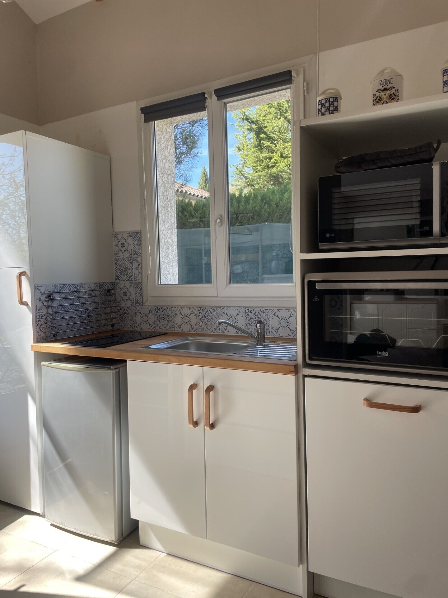 A kitchen with white cabinets, a built-in oven, a microwave, a sink, and a window with a view of greenery.
