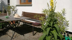 Eine Terrasse mit einer Holzbank, einem Tisch und Kübelpflanzen.