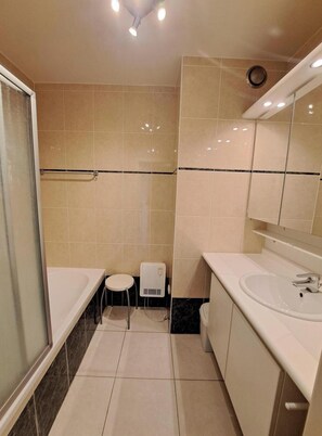 Ein modernes Badezimmer mit Badewanne, Waschbecken, Toilette und einem kleinen Hocker.