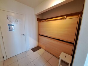 Ein Zimmer mit einer weißen Tür, einem Holzschrank, einem kleinen weißen Tisch und einem gefliesten Boden.