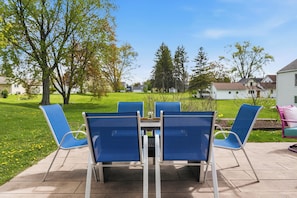 Un patio al aire libre con una mesa y cuatro sillas azules, rodeado de césped y árboles.