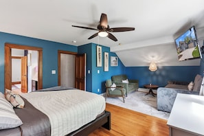 Un dormitorio con cama, ventilador de techo, televisor, una silla, un sofá y una mesita.