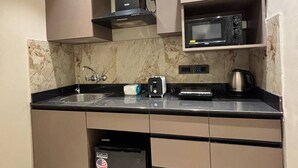 A compact kitchen with a microwave, toaster, and coffee maker on the counter, a dishwasher, and a built-in oven. - Studio Ethereal by VoyZen Privé (Greater Noida)