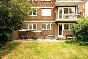 A two-story brick building with a small front yard, a bench, and a table. - The Garden Gatekeeper- by Out of Office Lifestyle (Greater London)