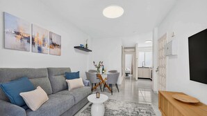 En moderne stue med en grå sofa, et sofabord og et spiseområde med stole og et bord.