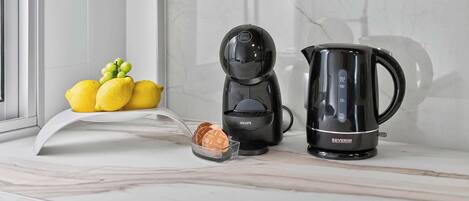 Una encimera de cocina con cafetera, hervidor y un cuenco de fruta.