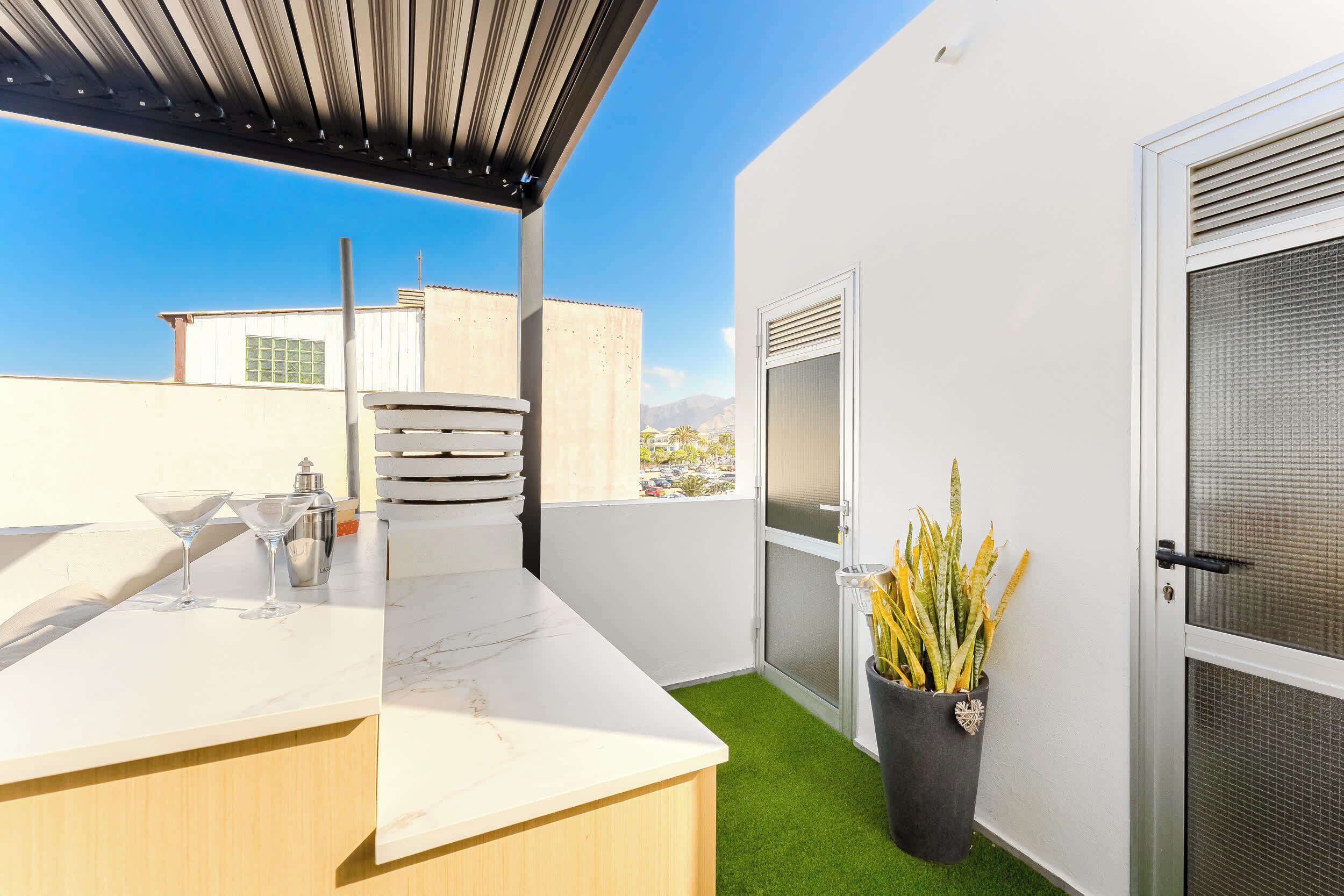 Eine Dachterrasse mit Barbereich, einer Tür mit Insektenschutzgitter und Blick auf die Stadt.