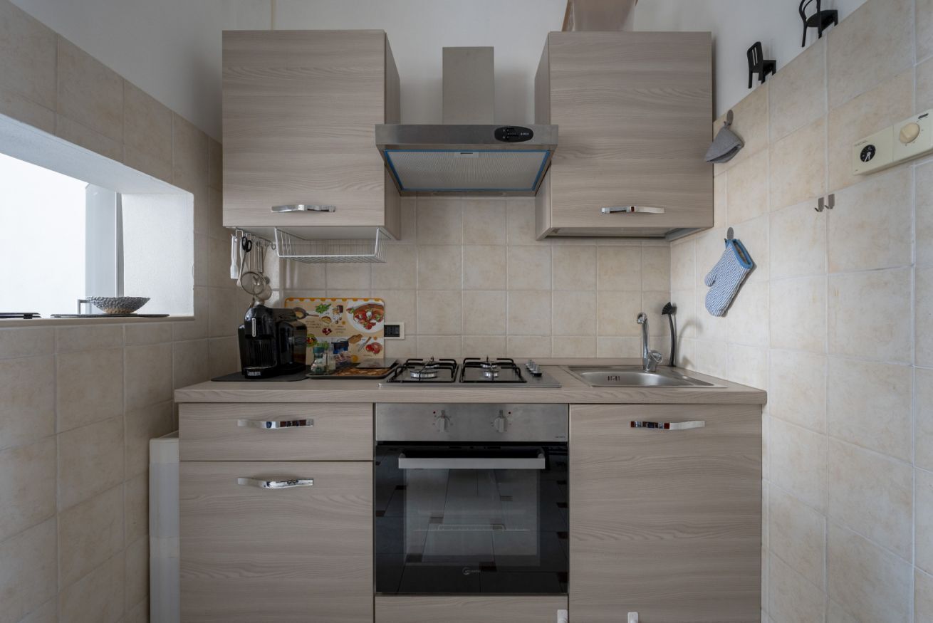 Una cucina moderna con piano cottura a gas, forno e lavello. Presenti mobili in legno e una finestra che offre luce naturale.