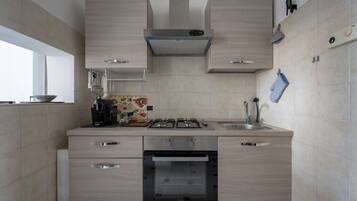 Una cucina moderna con piano cottura a gas, forno e lavello. Presenti mobili in legno e una finestra che offre luce naturale.