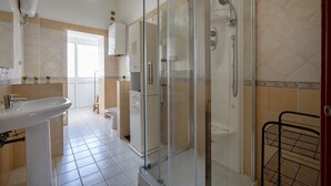 Et badeværelse med glasvæg omkring bruseren, et håndvask og et toilet.