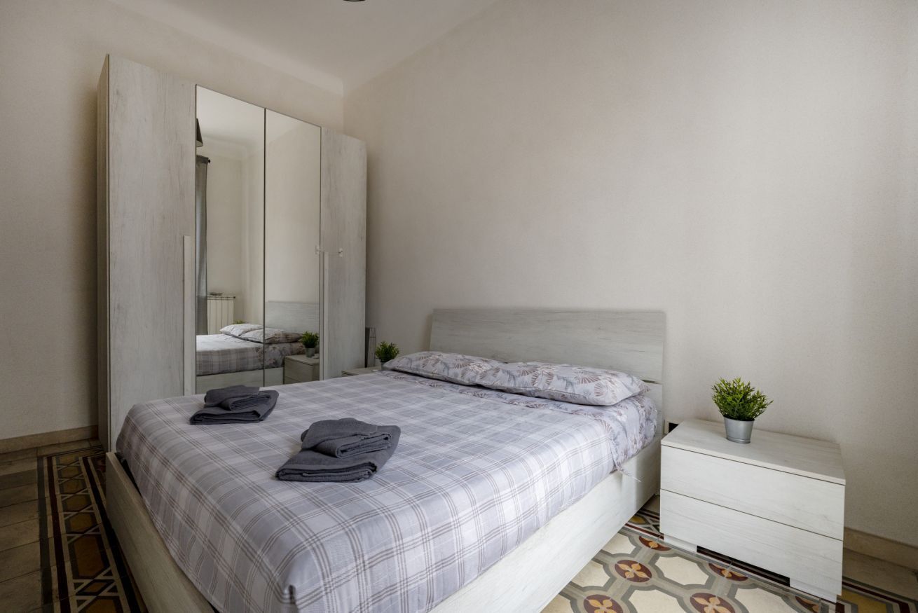 A bedroom with a bed, a nightstand, a mirror, and a potted plant.