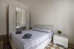 Ein Schlafzimmer mit einem Bett, einem Nachttisch, einem Spiegel und einer Zimmerpflanze.