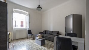 En moderne stue med en grå sofa, et spisebord med stole, en pendel og et stort vindue.
