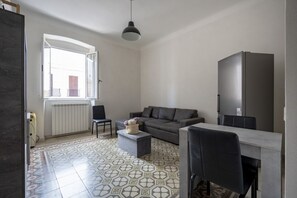 Un salon moderne avec un canapé gris, une table à manger avec des chaises, un luminaire suspendu et une grande fenêtre.