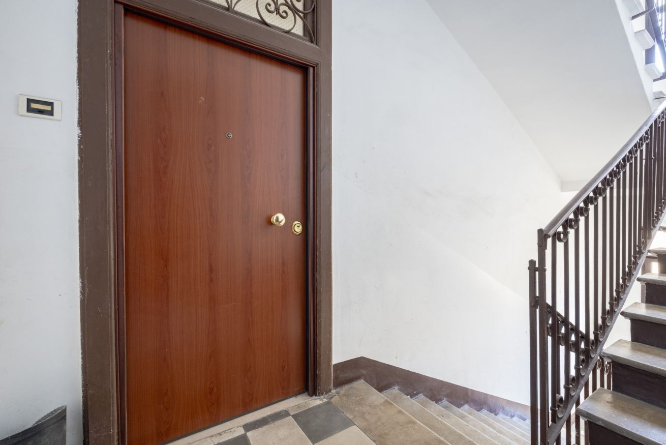 A wooden door with a brass handle, a metal staircase with a handrail, and a tiled floor.