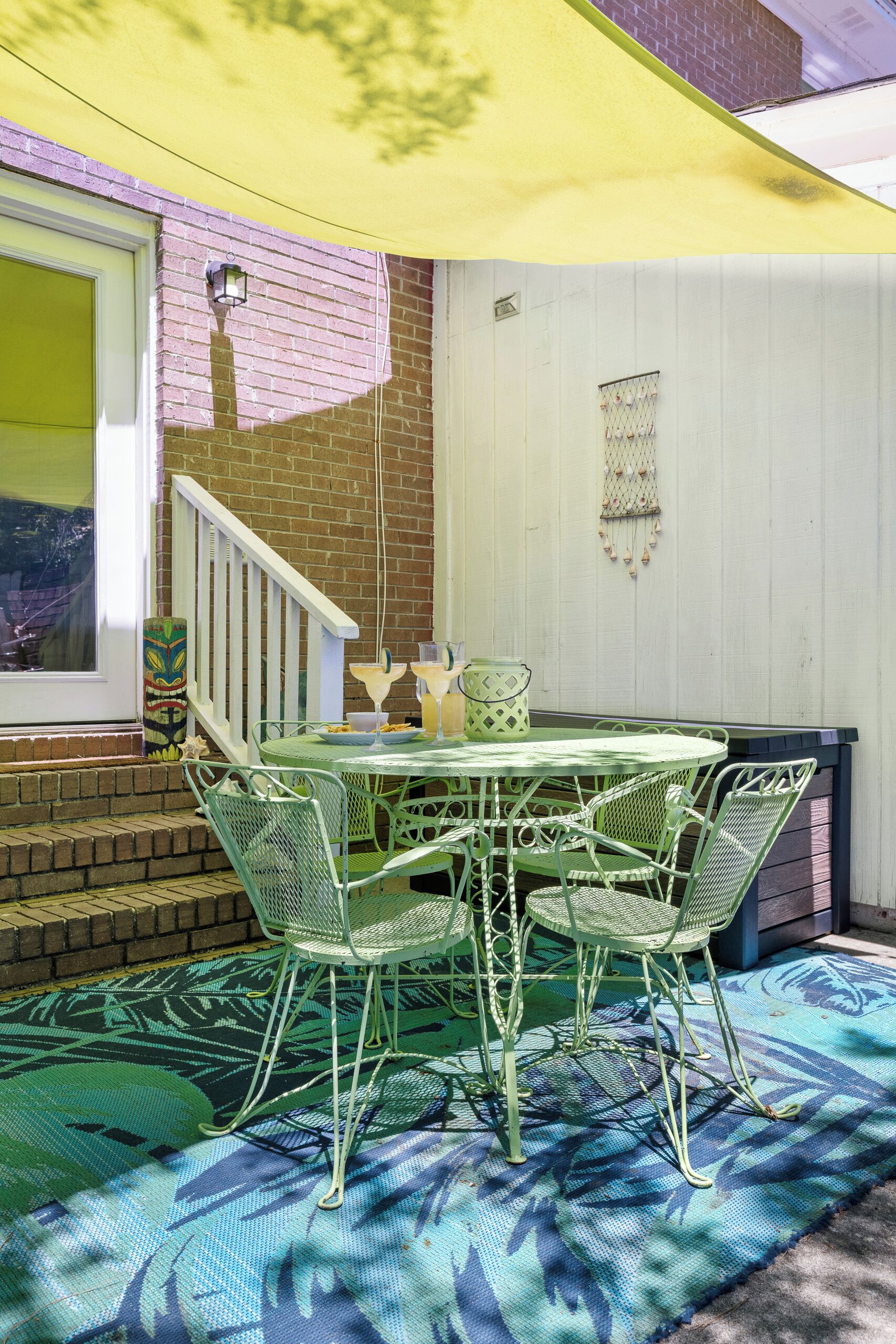 A patio with a table and chairs, a yellow awning, and a brick wall.