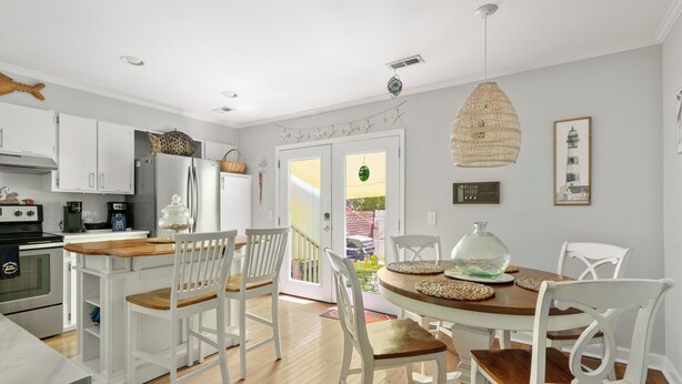 Una cocina con armarios blancos, encimera de madera y una zona de comedor con sillas blancas y mesa de madera.