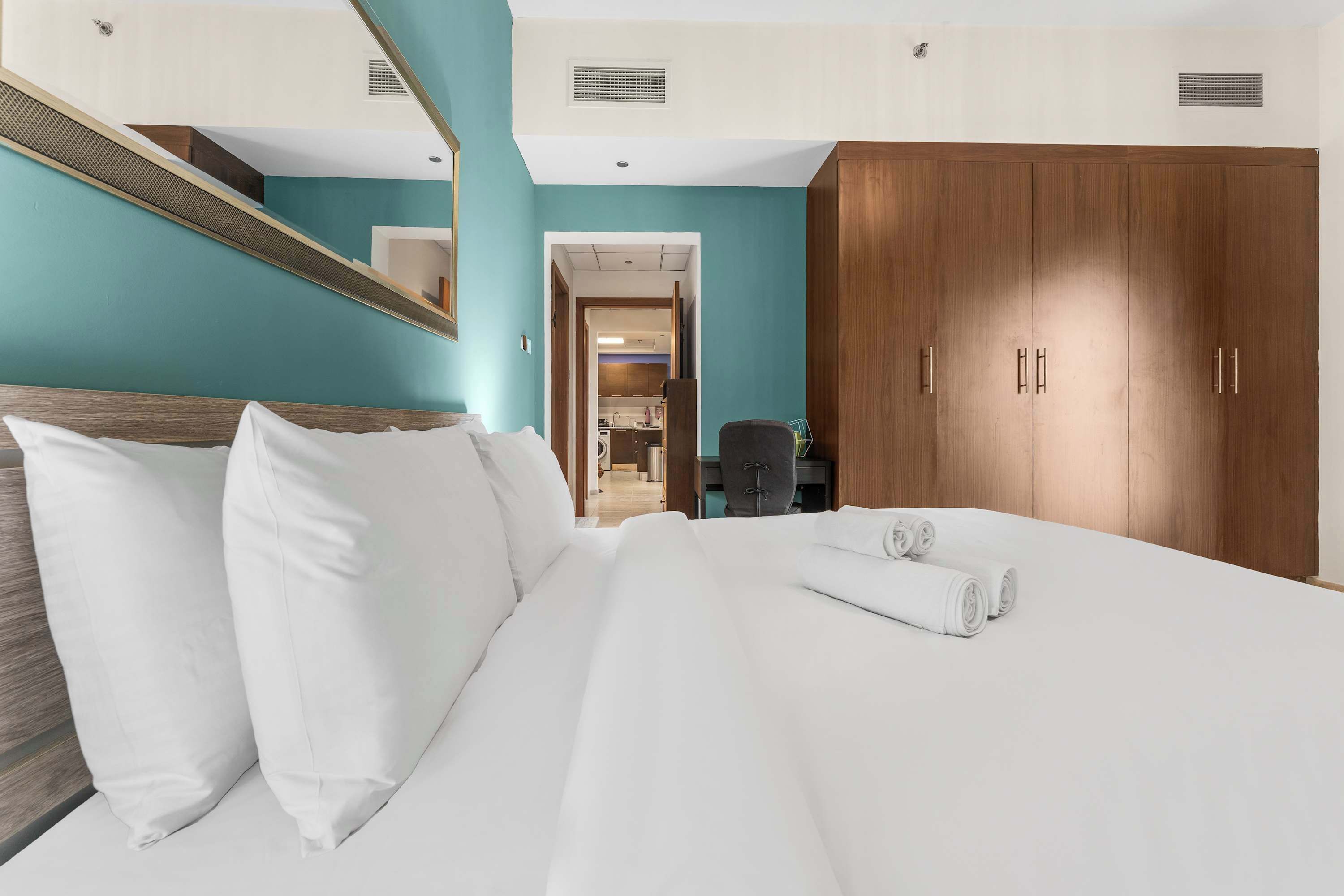 Une chambre d’hôtel avec un lit, une armoire en bois, un miroir et une vue sur le couloir.