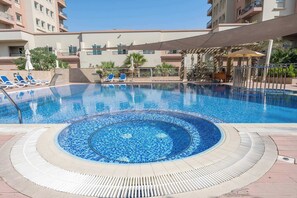 Ein Schwimmbecken mit Mosaikmuster, umgeben von Liegestühlen und einer schattigen Liegefläche.