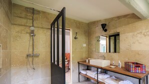 Un baño con ducha, lavabo, espejo y estante con toallas.