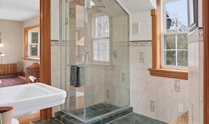 A bathroom with a glass shower enclosure, a bathtub, and a window.