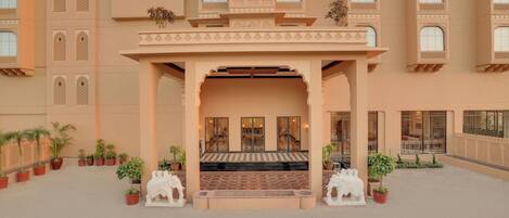 A hotel entrance with a checkered floor, potted plants, and two white statues.