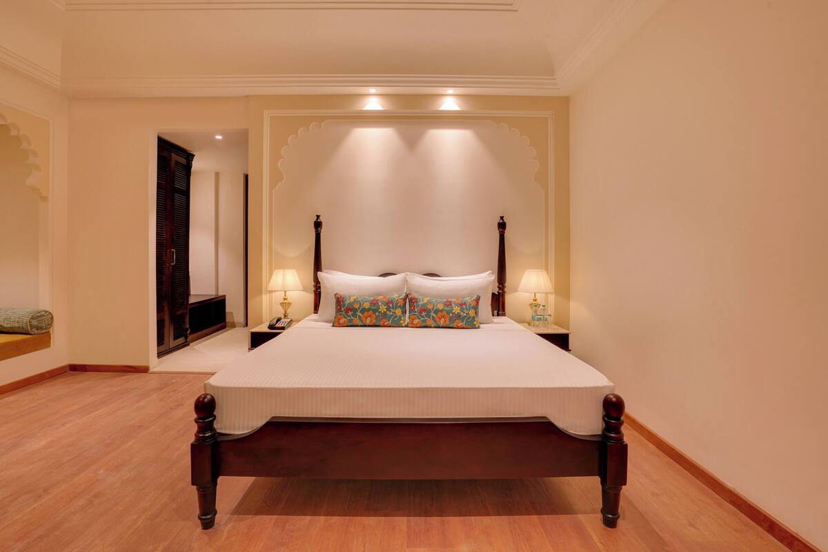 Uma cama grande com estrutura de madeira, duas luminárias de cabeceira e almofadas decorativas.