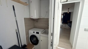Ein kleiner Hauswirtschaftsraum mit Waschmaschine, Besen und Ablagefläche.